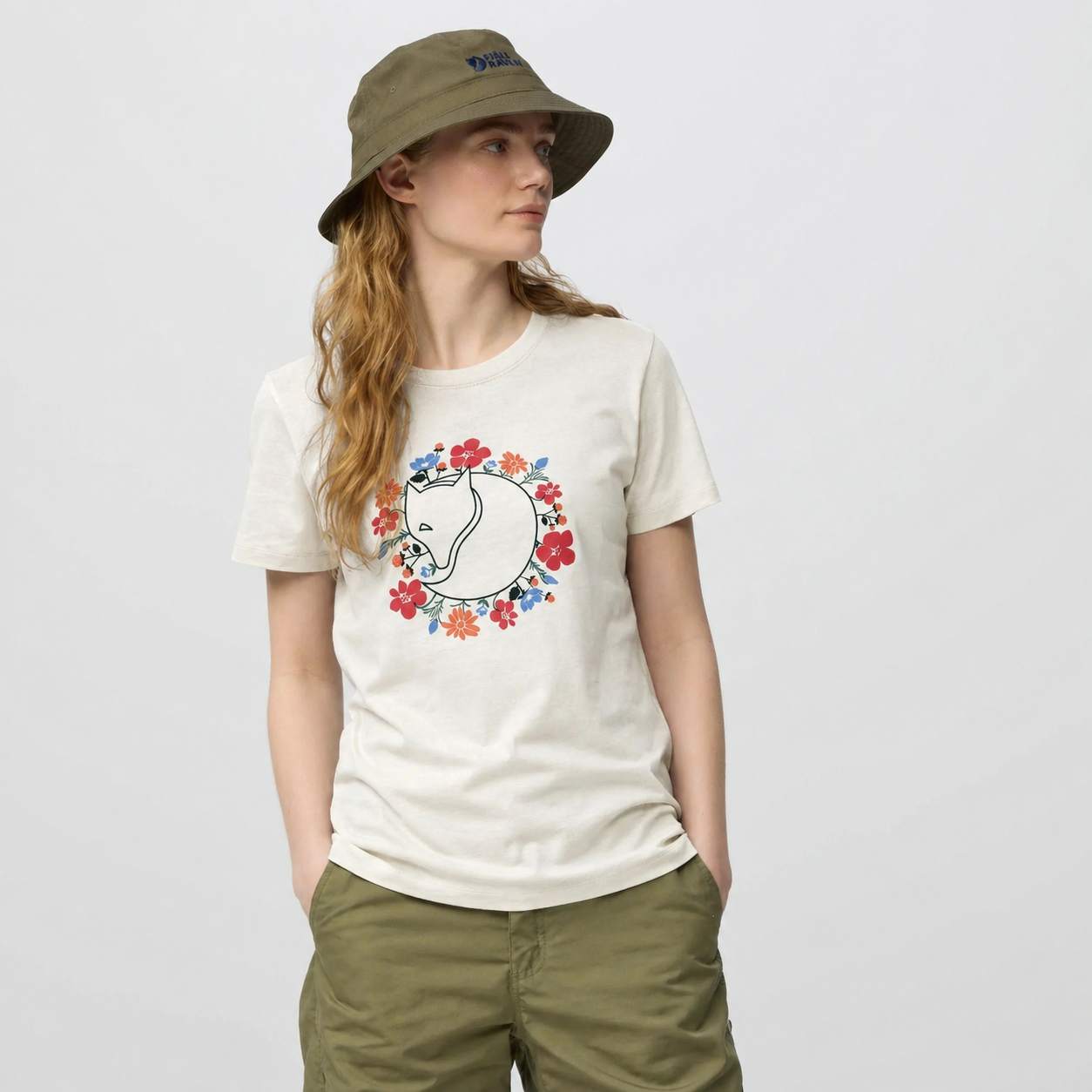 Model wearing a Fjallraven Fjällblomster Fox T-shirt with a colorful design and a hat on a plain background