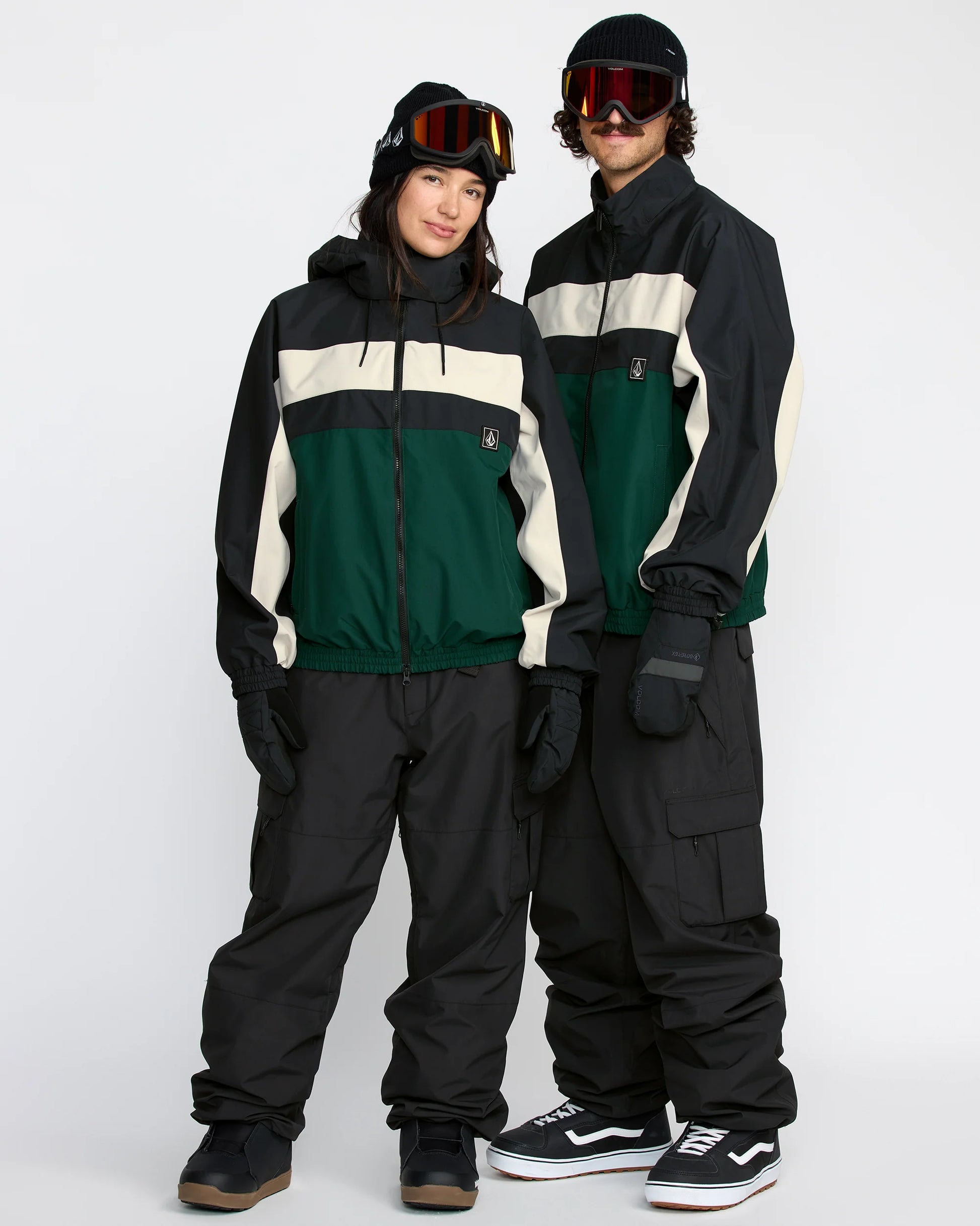 Two people wearing matching green and black Volcom ski suits on a white background