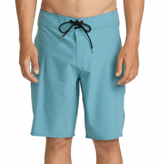 A man wearing light blue board shorts with a black drawstring, shown from the waist down against a plain white background.