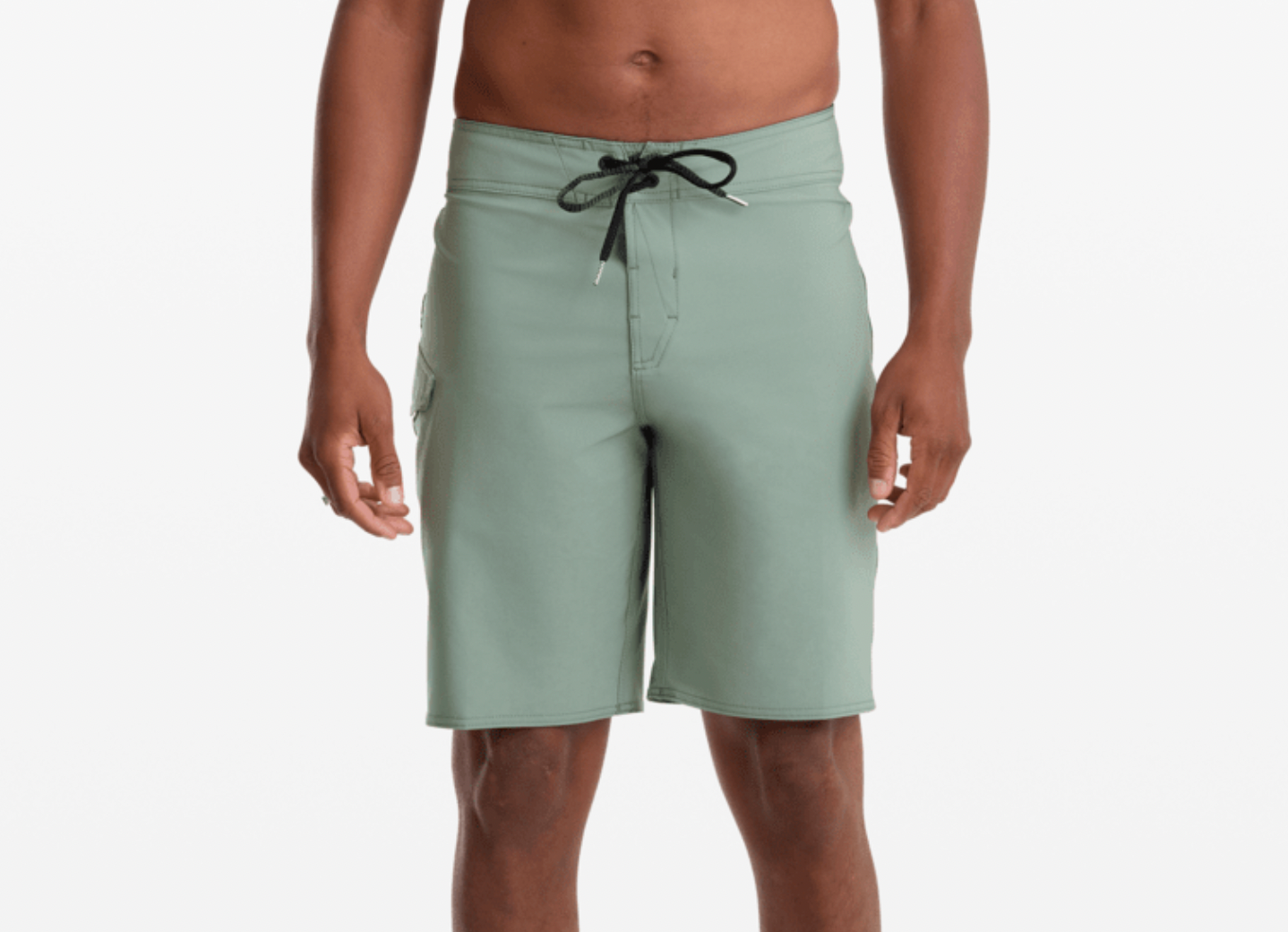 A man wearing sage green board shorts with a black drawstring, shown from the waist down against a light gray studio background.